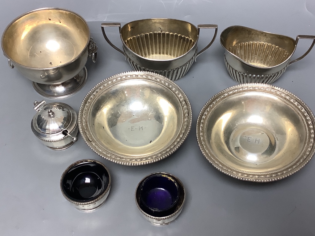 A pair of George V silver pedestal nut dishes, a small silver bowl with lion mask handles, a silver cream and sugar and a three piece silver condiment set